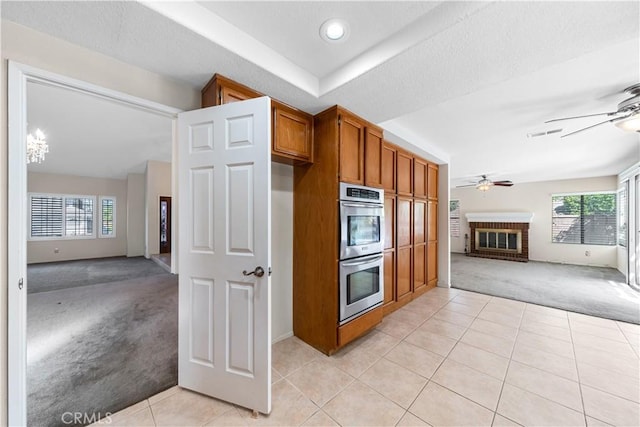 kitchen with light tile patterned floors, brown cabinetry, double oven, light colored carpet, and open floor plan