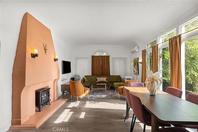 dining area with vaulted ceiling, a textured ceiling, a wall mounted air conditioner, and wood finished floors