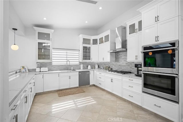 kitchen featuring decorative backsplash, stainless steel appliances, white cabinetry, wall chimney exhaust hood, and a sink