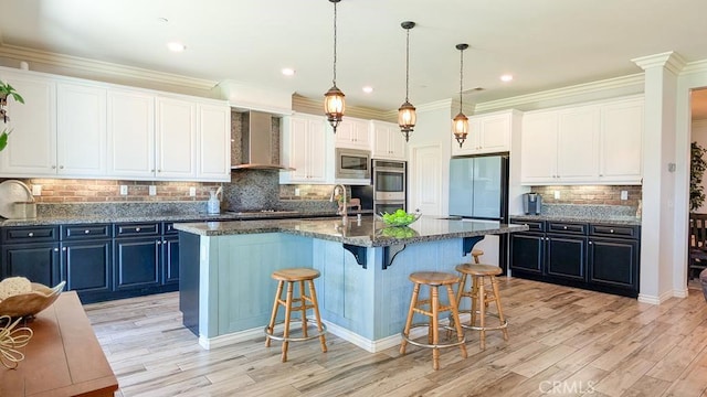 kitchen featuring wall chimney range hood, white cabinets, appliances with stainless steel finishes, crown molding, and a kitchen breakfast bar