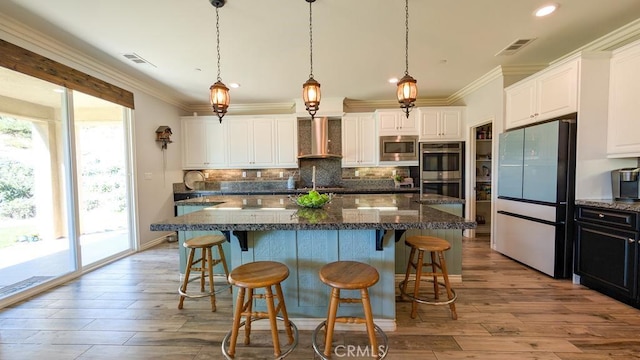 kitchen with crown molding, wall chimney range hood, visible vents, and appliances with stainless steel finishes