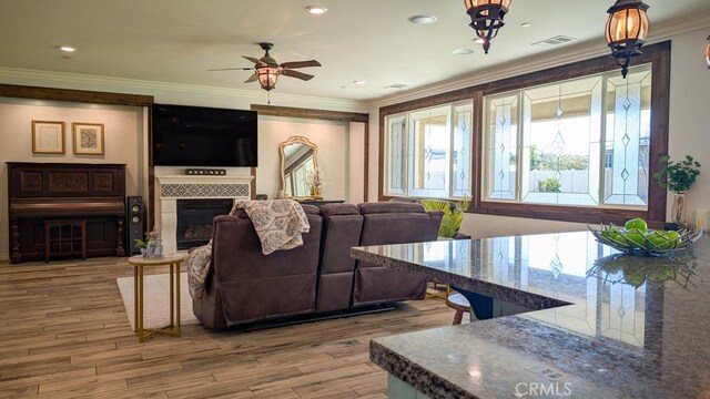 living room featuring visible vents, crown molding, a tile fireplace, wood finished floors, and a ceiling fan