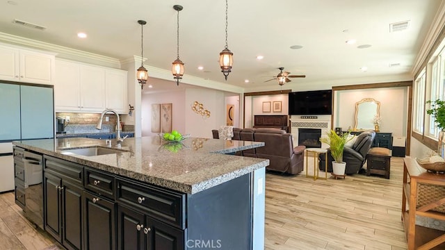 kitchen featuring a glass covered fireplace, visible vents, a sink, white cabinetry, and light wood-type flooring