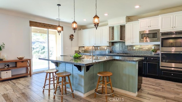 kitchen featuring tasteful backsplash, wall chimney range hood, a breakfast bar area, ornamental molding, and stainless steel appliances