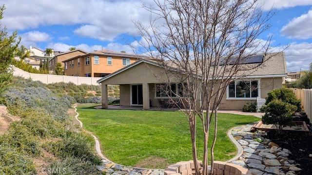 rear view of property featuring solar panels, a fenced backyard, stucco siding, a patio area, and a lawn