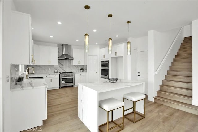 kitchen with a sink, wall chimney range hood, backsplash, appliances with stainless steel finishes, and light wood finished floors