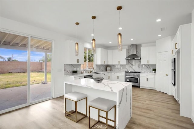 kitchen with a sink, tasteful backsplash, light wood-style floors, appliances with stainless steel finishes, and wall chimney range hood