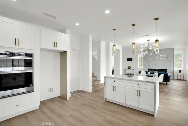 kitchen featuring open floor plan, white cabinets, light wood-type flooring, and stainless steel double oven