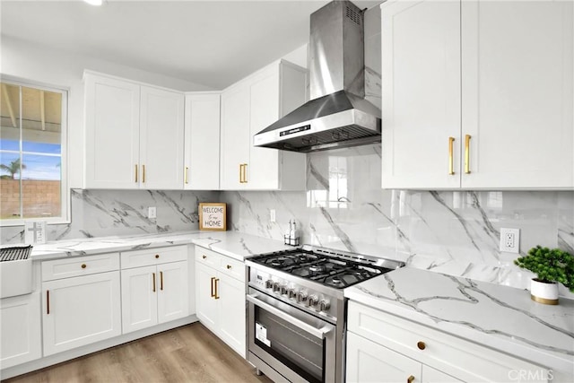 kitchen with high end stove, white cabinetry, and wall chimney range hood