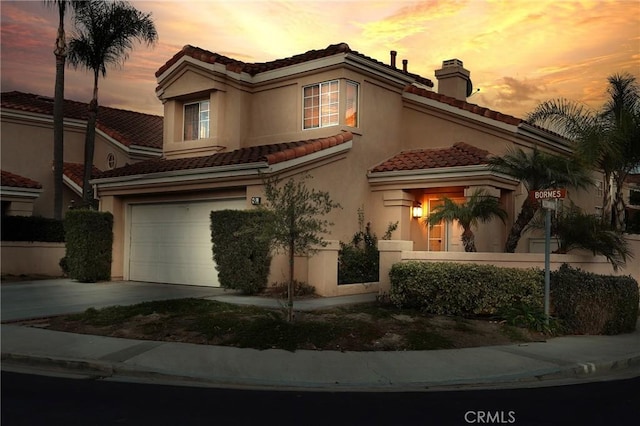 mediterranean / spanish house with stucco siding, driveway, an attached garage, a chimney, and a tiled roof