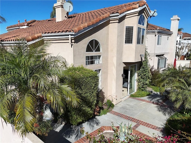 exterior space featuring stucco siding, a tiled roof, and a chimney