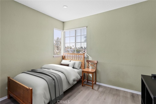 bedroom with baseboards, wood finished floors, and a textured wall