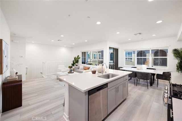 kitchen with stainless steel dishwasher, gray cabinets, light wood finished floors, and a sink