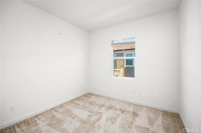 spare room featuring light carpet and baseboards