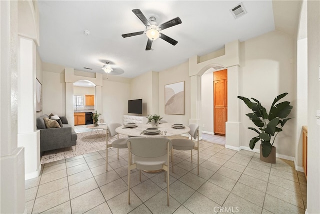 dining space featuring light tile patterned floors, a ceiling fan, visible vents, baseboards, and arched walkways