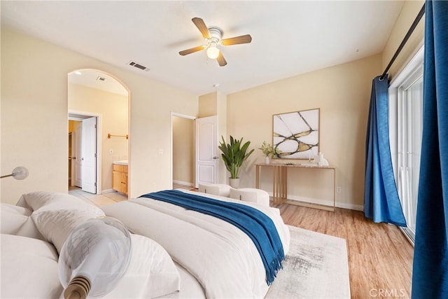 bedroom featuring visible vents, baseboards, ensuite bath, arched walkways, and light wood-style floors