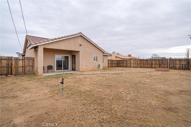 back of house featuring a patio area, a tiled roof, a fenced backyard, and stucco siding