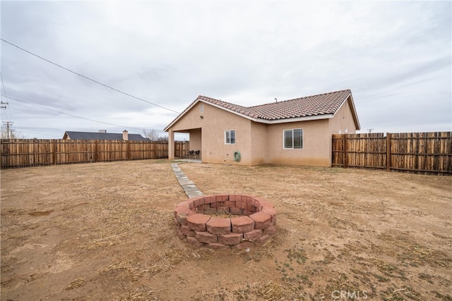 back of property featuring a tiled roof, stucco siding, a fenced backyard, and an outdoor fire pit