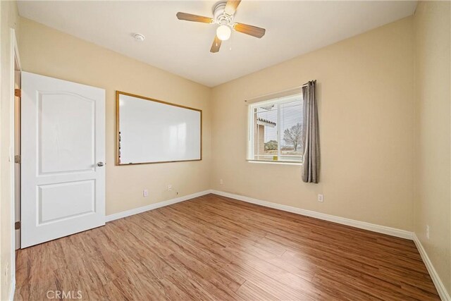 empty room with a ceiling fan, wood finished floors, and baseboards