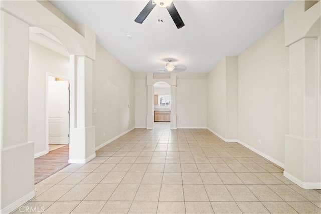 spare room featuring light tile patterned floors, baseboards, arched walkways, and ceiling fan