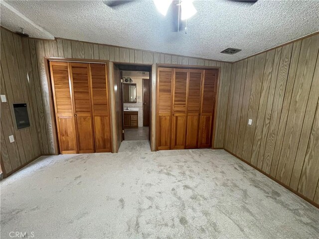 1111 Taos Dr, Barstow, CA 92311 - unfurnished bedroom featuring carpet floors, wood walls, multiple closets, a textured ceiling, and ceiling fan
