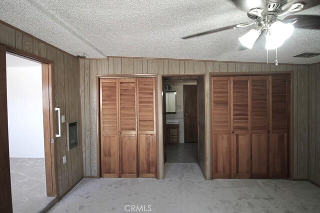 1111 Taos Dr, Barstow, CA 92311 - unfurnished bedroom featuring wooden walls, carpet flooring, two closets, a textured ceiling, and ornamental molding