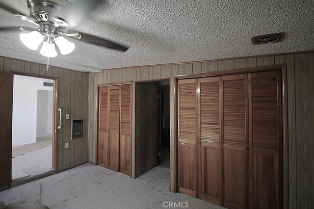 1111 Taos Dr, Barstow, CA 92311 - unfurnished bedroom with wood walls, multiple closets, a textured ceiling, light carpet, and ceiling fan