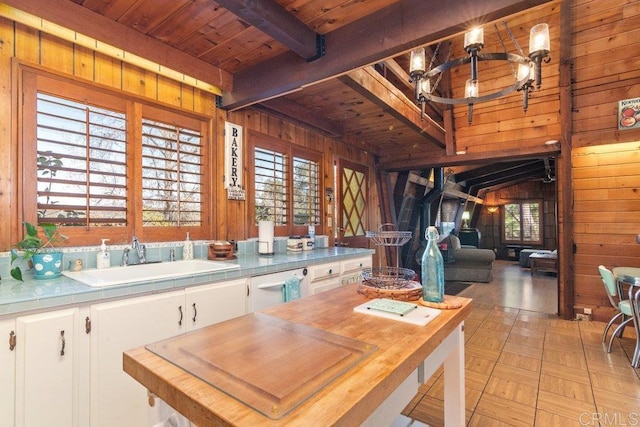 kitchen featuring wooden walls, beamed ceiling, tile countertops, dishwasher, and a sink