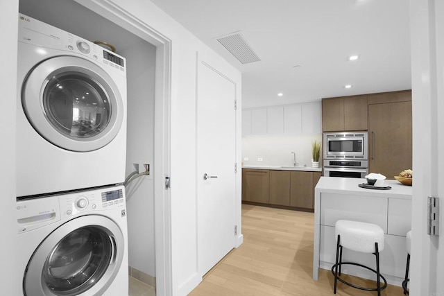 laundry room with stacked washer and clothes dryer, a sink, visible vents, light wood-style flooring, and laundry area