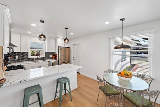 kitchen with a peninsula, a sink, stainless steel appliances, white cabinets, and tasteful backsplash