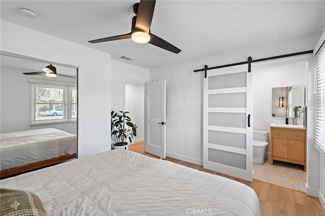 bedroom with a ceiling fan, visible vents, ensuite bathroom, a barn door, and light wood-type flooring