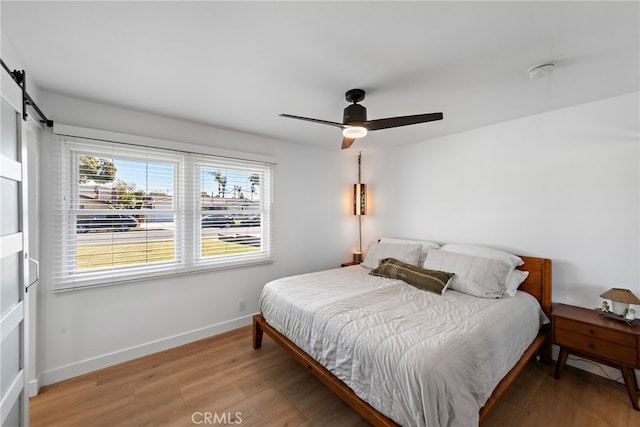 bedroom with ceiling fan, a barn door, baseboards, and wood finished floors