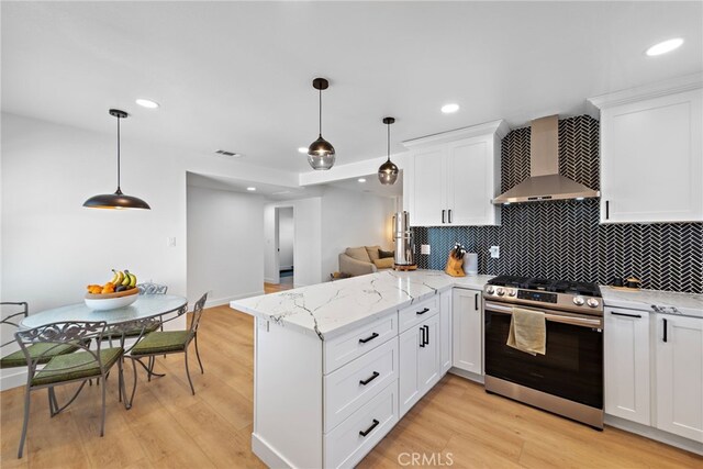 kitchen featuring visible vents, stainless steel range, a peninsula, wall chimney exhaust hood, and white cabinets