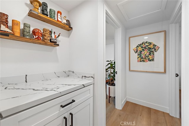 interior space featuring light wood-type flooring, open shelves, light stone counters, white cabinetry, and baseboards