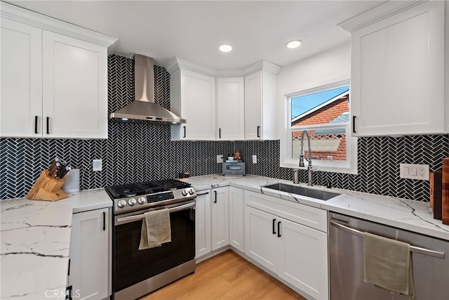 kitchen featuring white cabinets, appliances with stainless steel finishes, wall chimney range hood, and a sink