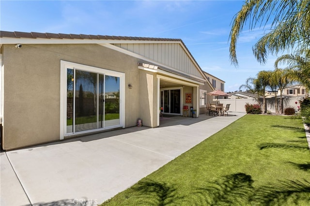 rear view of property featuring a patio, a lawn, fence, and stucco siding