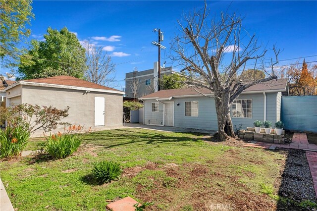 rear view of house featuring an outbuilding, a yard, and fence