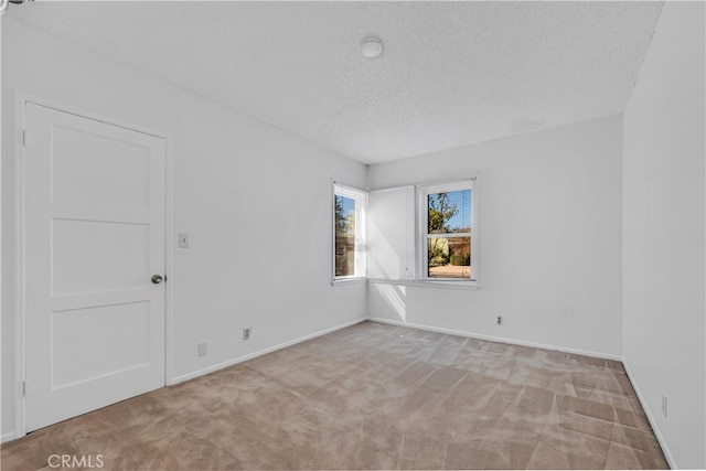 carpeted spare room featuring a textured ceiling and baseboards