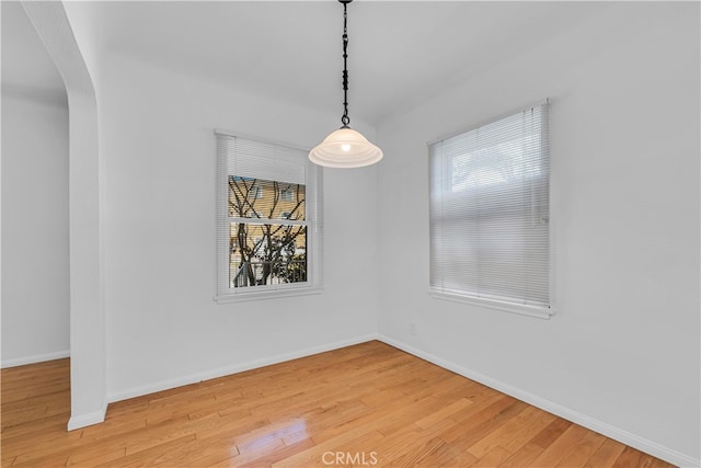 unfurnished room featuring baseboards, arched walkways, and light wood-style flooring