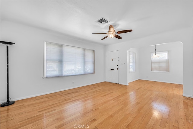 unfurnished living room featuring visible vents, light wood-style flooring, arched walkways, baseboards, and ceiling fan