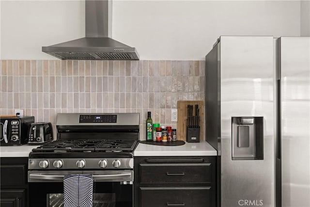 kitchen featuring wall chimney range hood, tasteful backsplash, dark cabinetry, appliances with stainless steel finishes, and light countertops