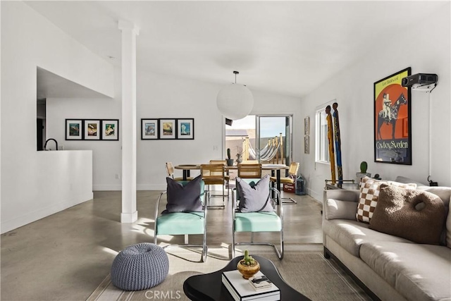 living room featuring lofted ceiling, decorative columns, baseboards, and concrete flooring