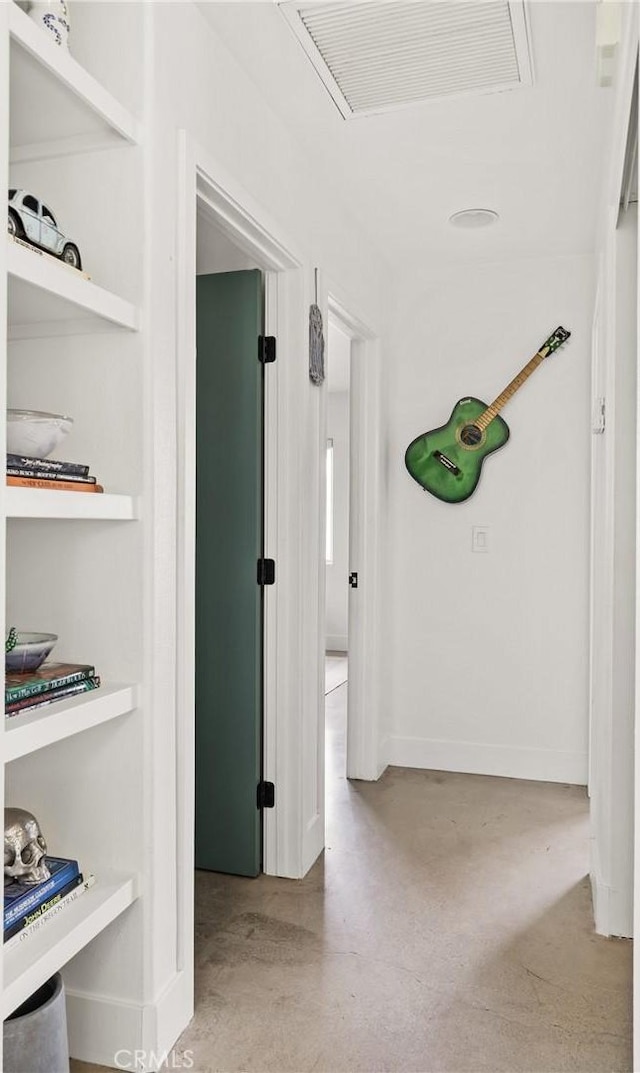 hallway featuring built in features, visible vents, baseboards, and finished concrete flooring