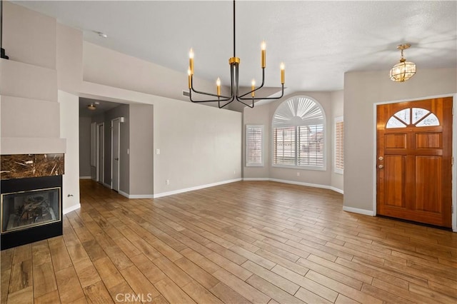 entryway featuring baseboards, an inviting chandelier, light wood-style flooring, and a high end fireplace