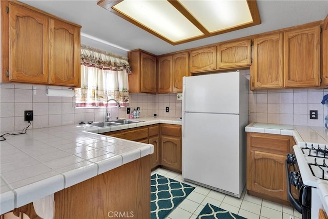 kitchen featuring freestanding refrigerator, a sink, decorative backsplash, range with gas cooktop, and brown cabinets