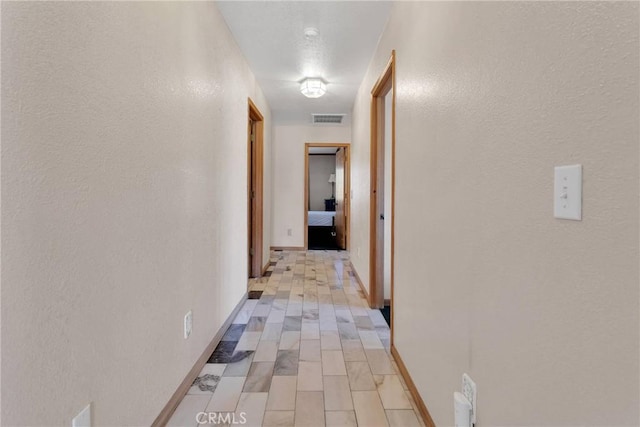 corridor featuring visible vents, baseboards, and a textured wall