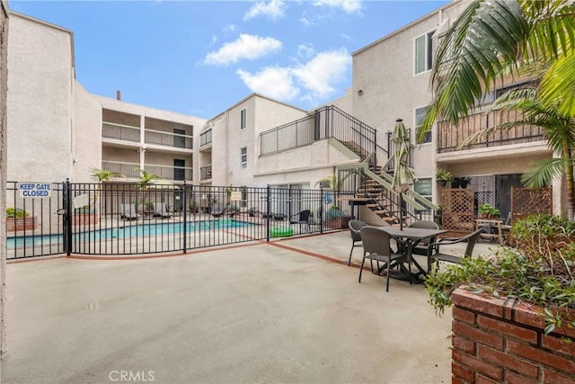 view of patio / terrace with a community pool, stairs, and fence