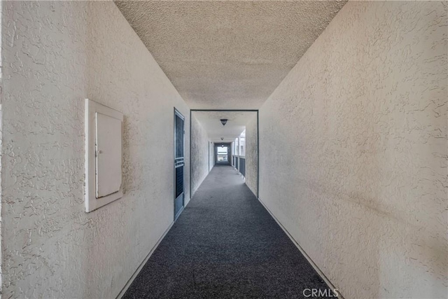 hallway featuring electric panel, carpet flooring, a textured ceiling, and a textured wall