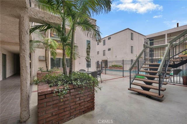 view of patio featuring stairs, a community pool, and fence