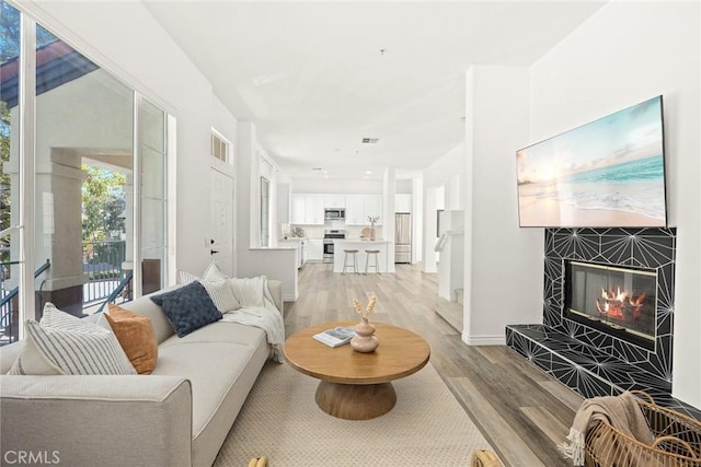 living room featuring a tiled fireplace, visible vents, baseboards, and light wood-style floors